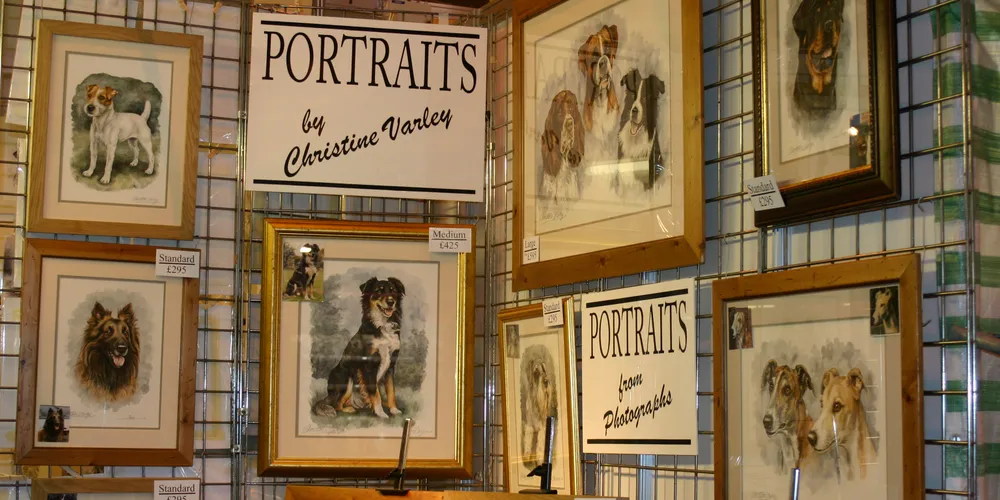 Framed pet portraits on a show stand, with signs reading Portraits by Christine Varley and Portraits from Photographs