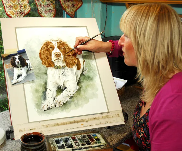 Christine Varley painting a springer spaniel at her easel, the owner's photo taped beside it