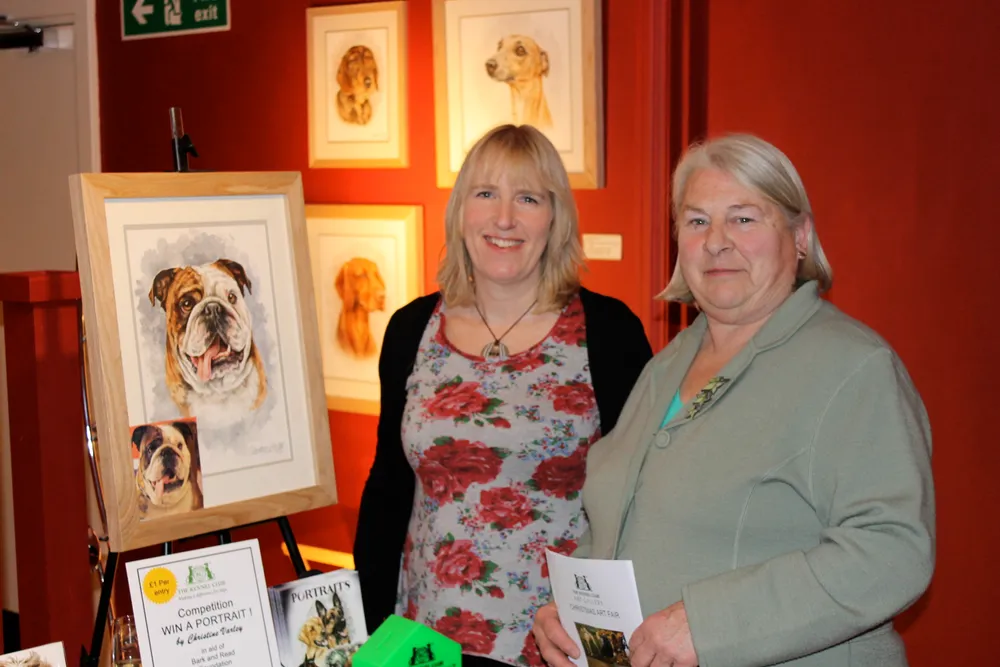 Christine with Pat Sutton of the Kennel Club Gallery board, beside her framed paintings