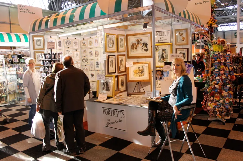 Visitors browsing a show stand hung with framed portraits, with a sign reading Portraits by Christine Varley