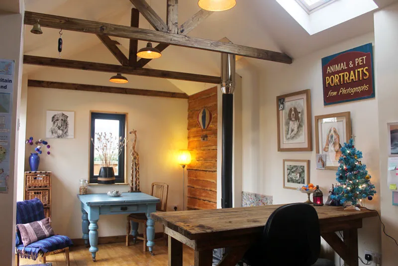 Christine's studio: wooden beams and a skylight, a pale blue desk, framed portraits on the walls and a sign reading Animal and Pet Portraits